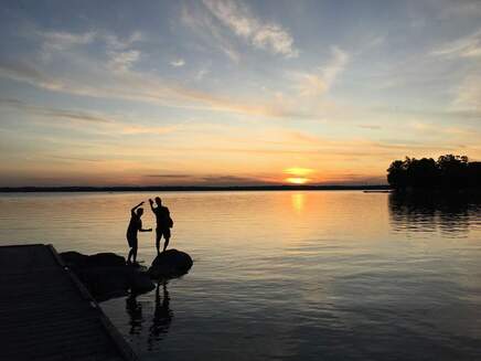 Sons in silhouette waving at sunset on Lake Simcoe.